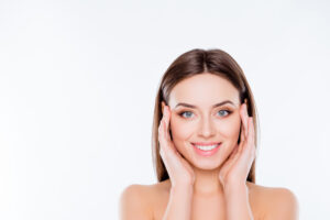 Woman smiles, holding her hands on either side of her face to emphasize her youthful look after a brow lift