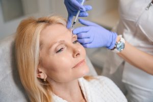 Woman receiving a BOTOX injection in the forehead from a provider wearing blue medical gloves.